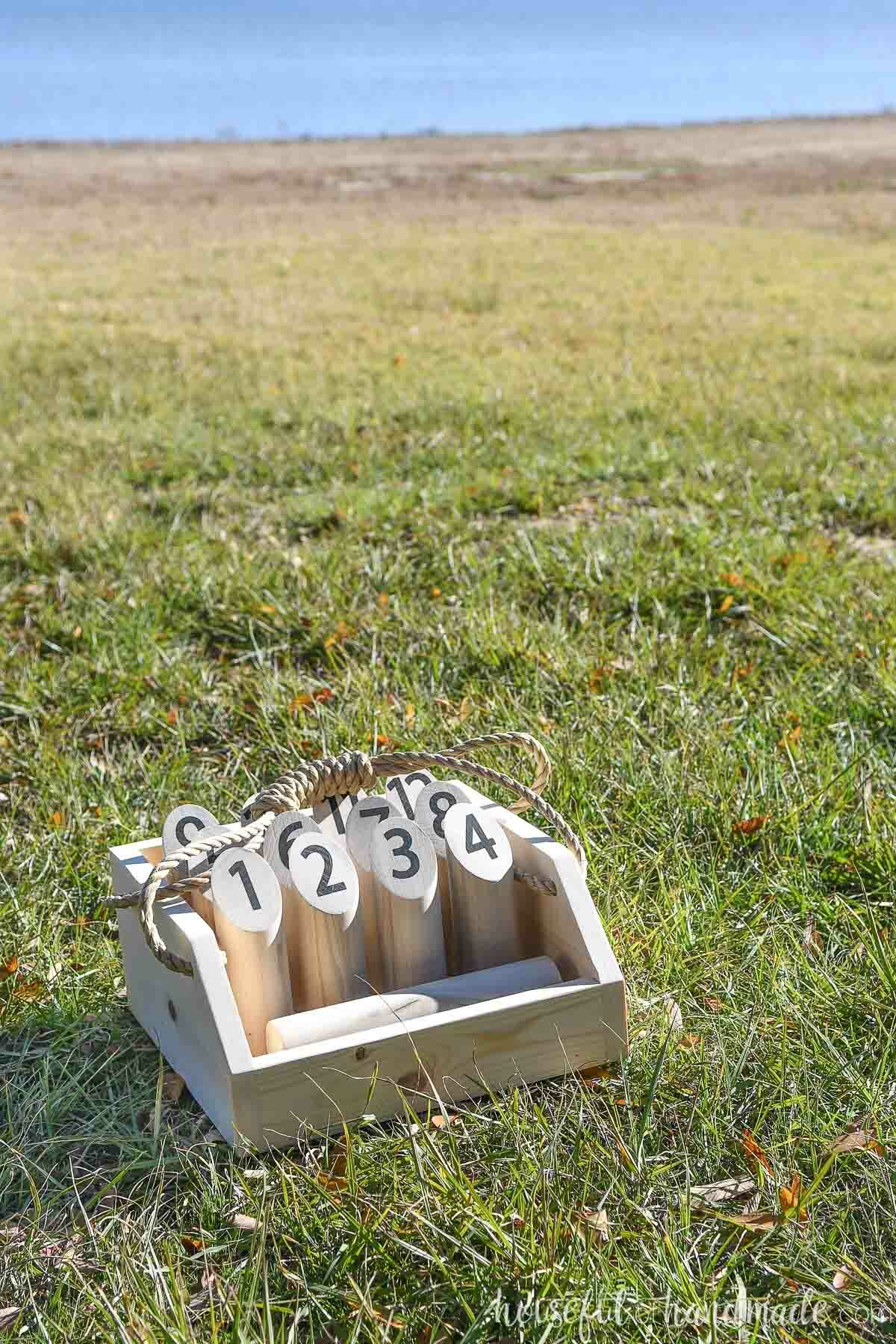 Wood Mölkky set in a custom carrier with a handle sitting on a lawn in front of a lake.