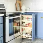 DIY pull out spice rack cabinet with 3 shelves in a kitchen with blue cabinets.