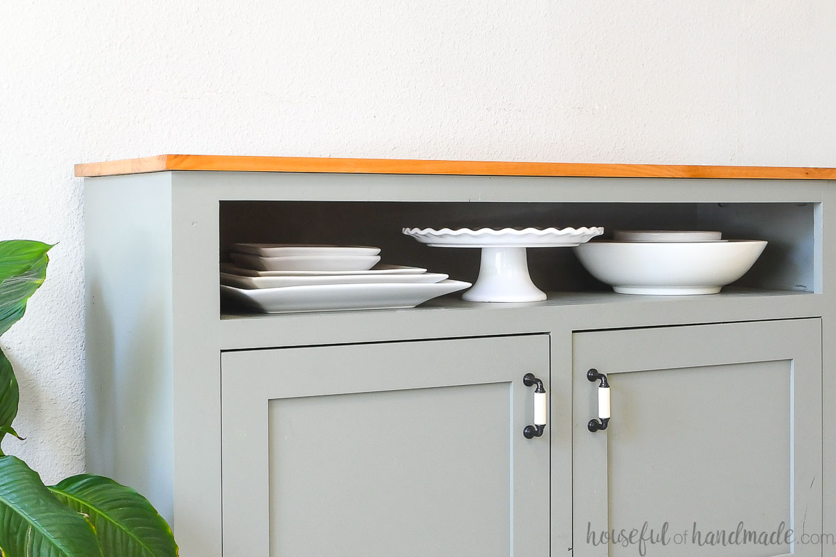 Narrow shelf above the cabinet in a sideboard storing large serving trays, bowls and a cake plate. 