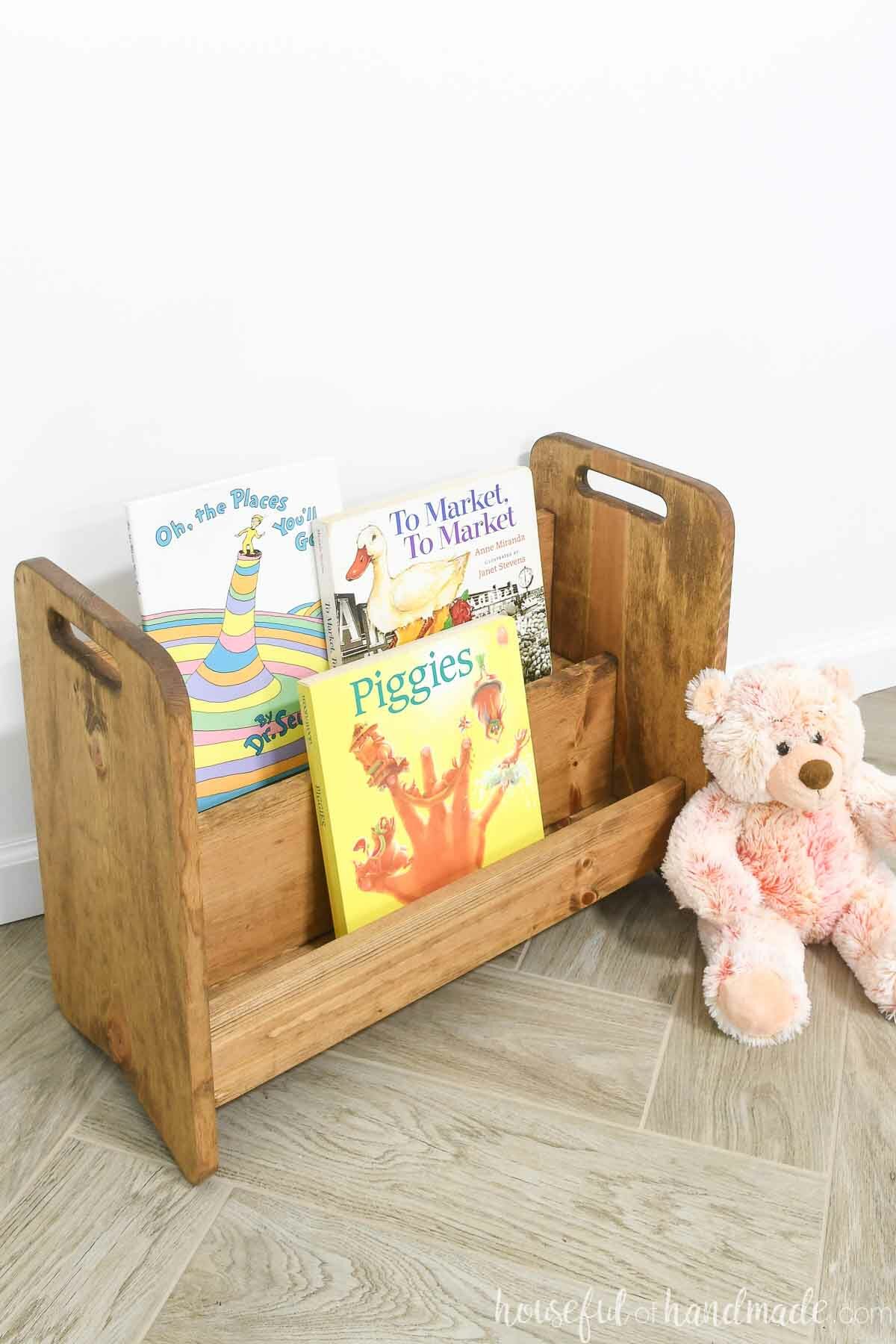 Three books on a montessori style bookcase sitting on a wood tile florr. 