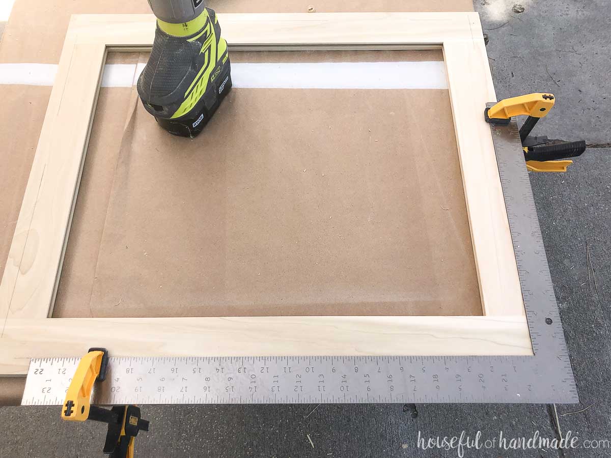 A framing square clamped to the door frame on the marked perimeter line. 
