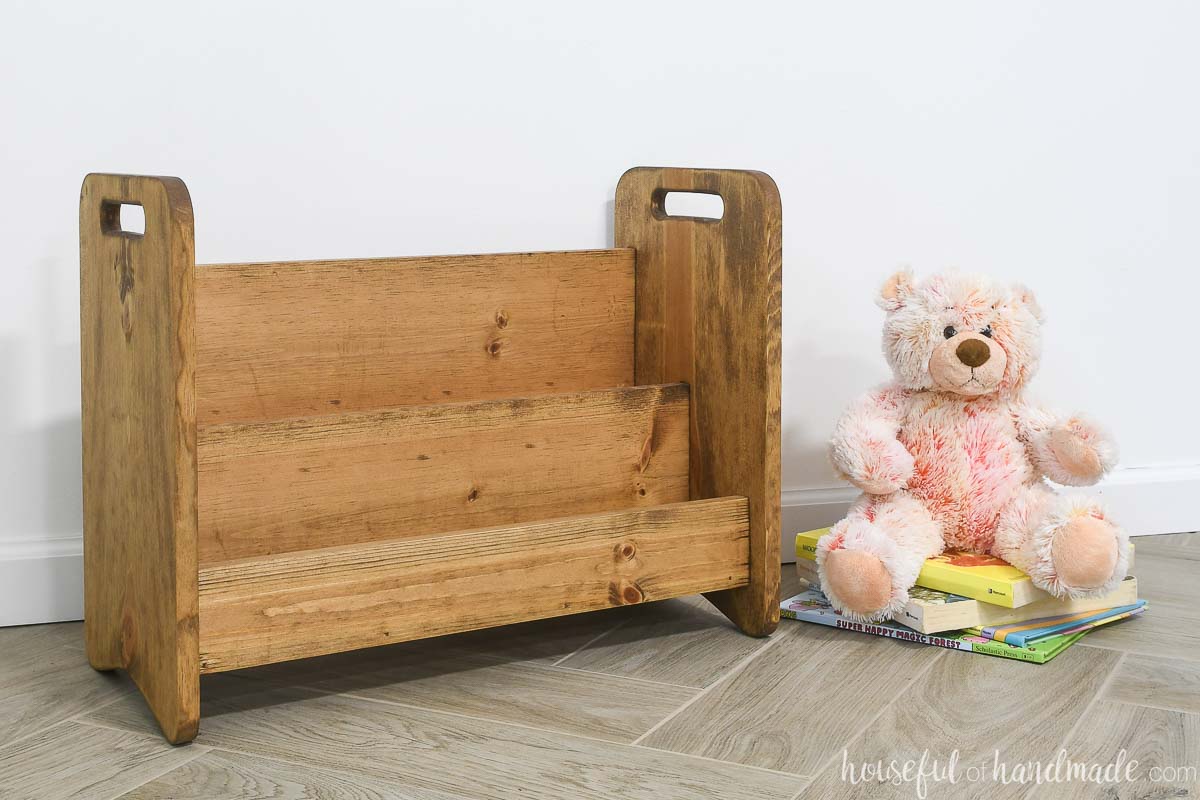 Empty toddle bookcase stained medium wood tones next to a stuffed animal.
