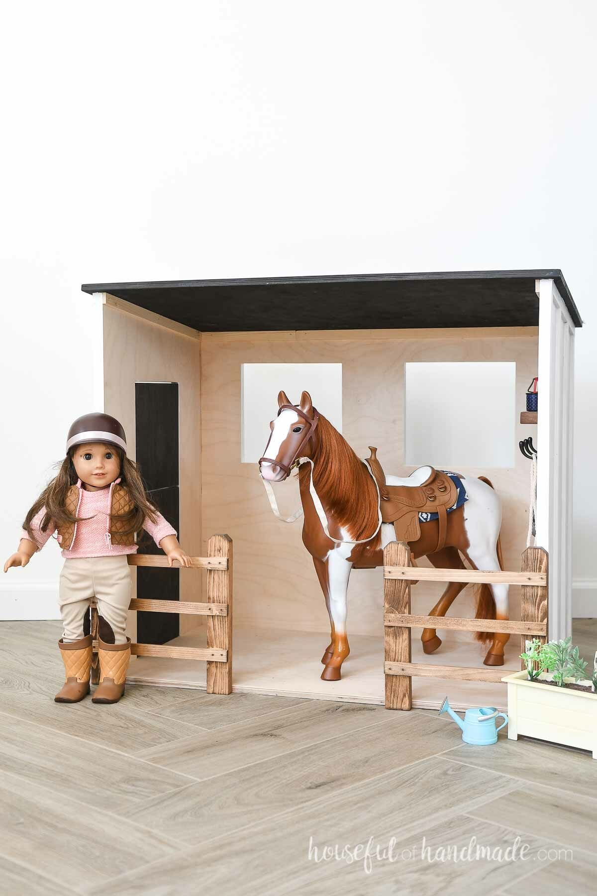 Inside of the DIY toy barn with fences on the sides and toy horse inside next to an American Girl doll. 