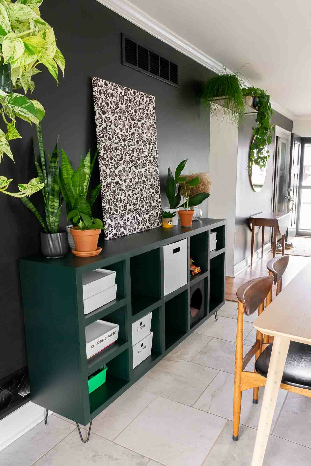Dark green painted DIY cube storage shelf with hairpin legs on a black wall in a dining room. 