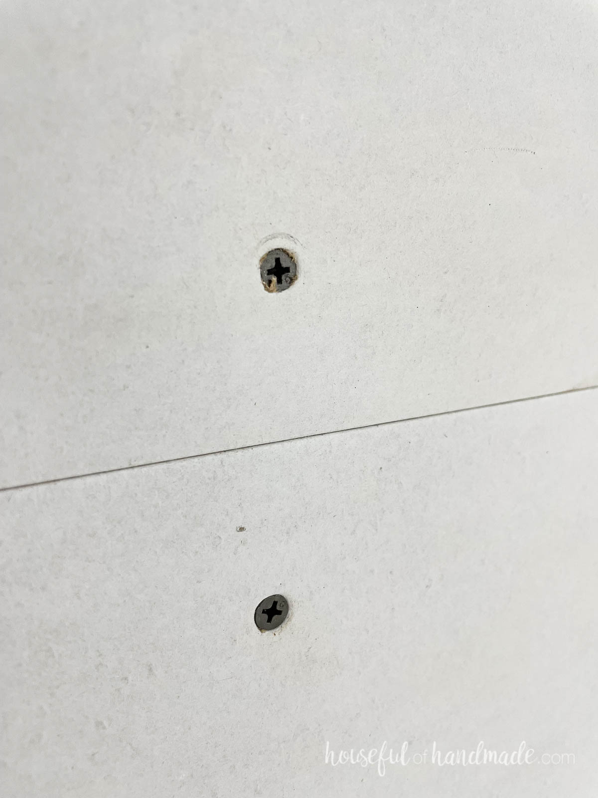 Two drywall screws in a sheet of drywall showing the correct depth of countersinking. 