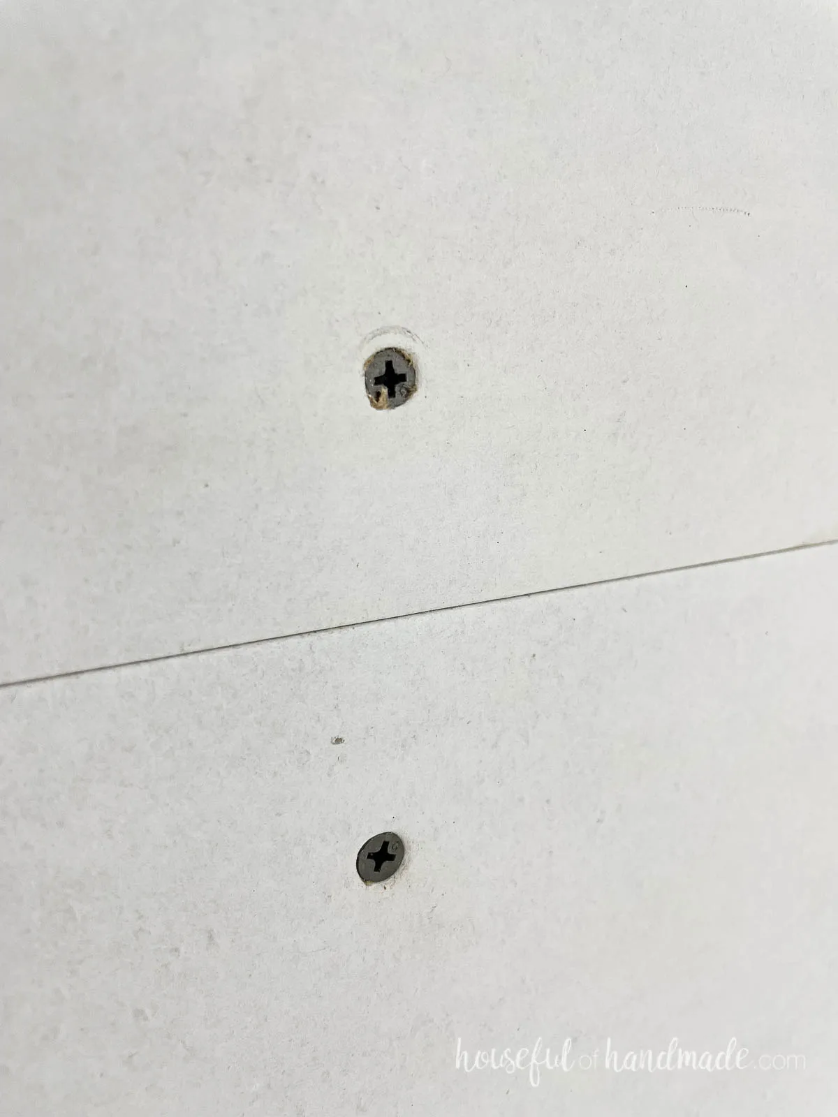 Two drywall screws in a sheet of drywall showing the correct depth of countersinking. 