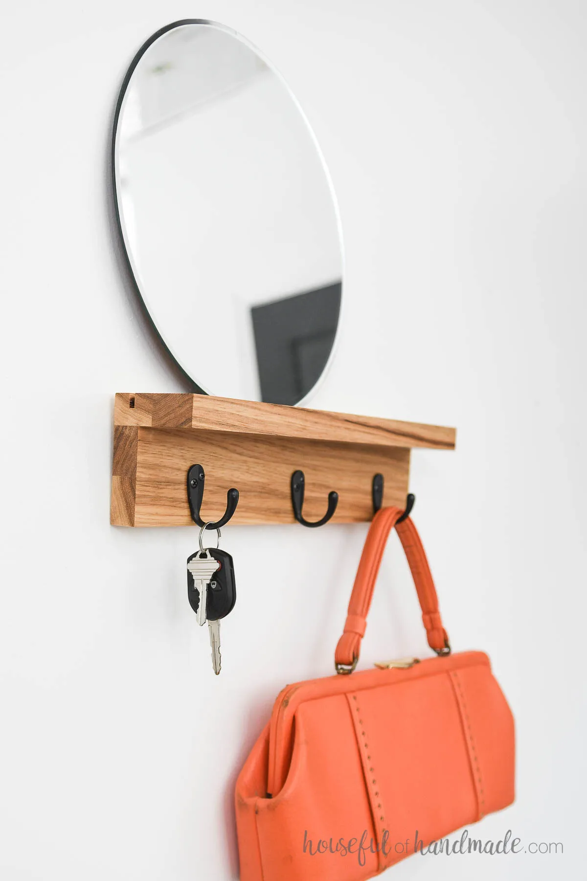 DIY entryway shelf with 3 hooks and a round mirror holding keys and a purse.