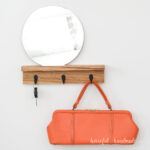 Wood entryway shelf with a mirror on top and hooks for keys and bags below.