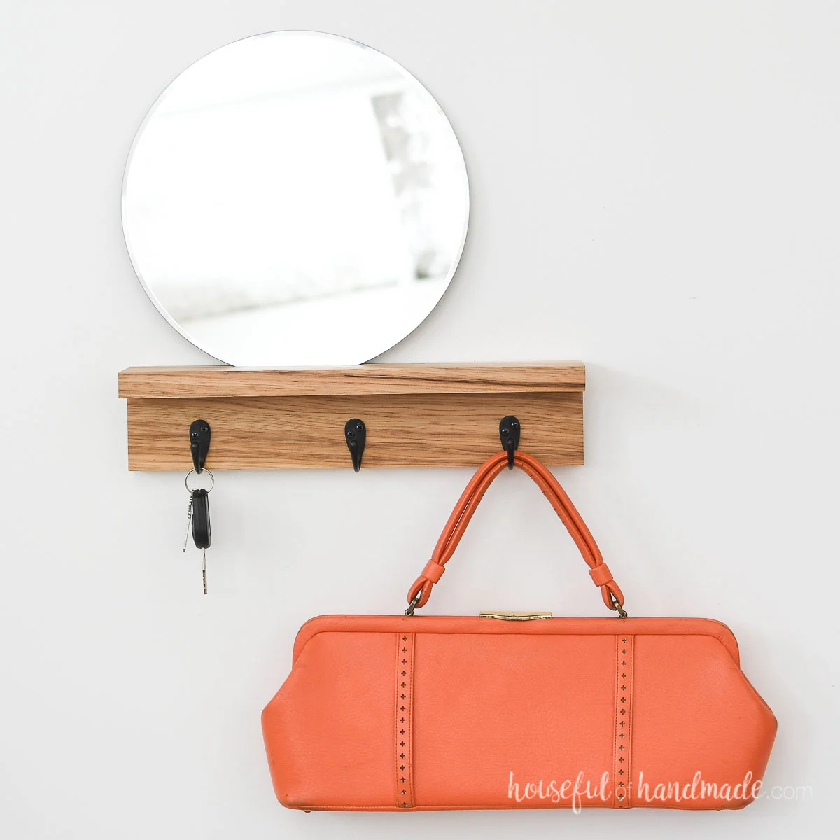 Wood entryway shelf with a mirror on top and hooks for keys and bags below.