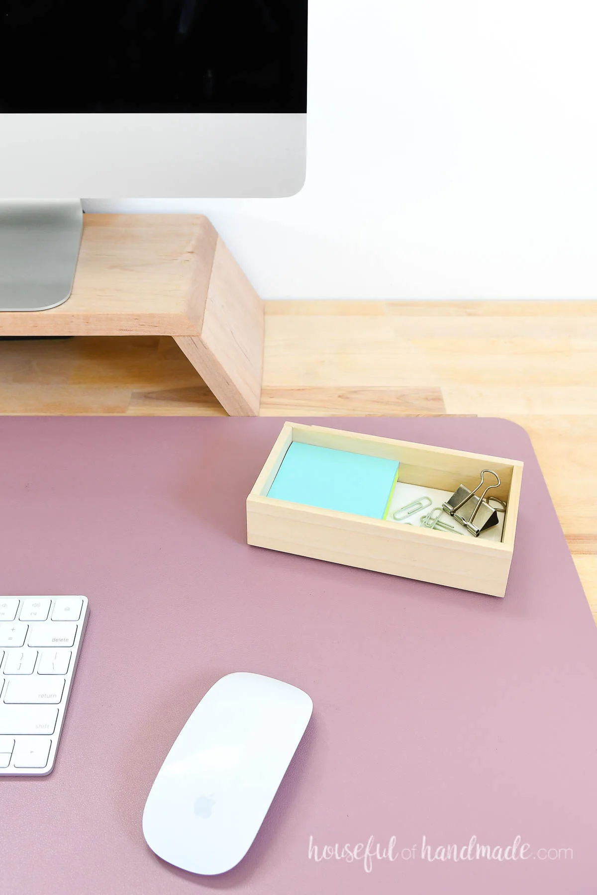 Desktop with a pink desk protector and small organizing tray made from scraps or wood and tile. 