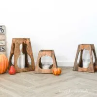 DIY fall lanterns made from wood with pumpkins around them.