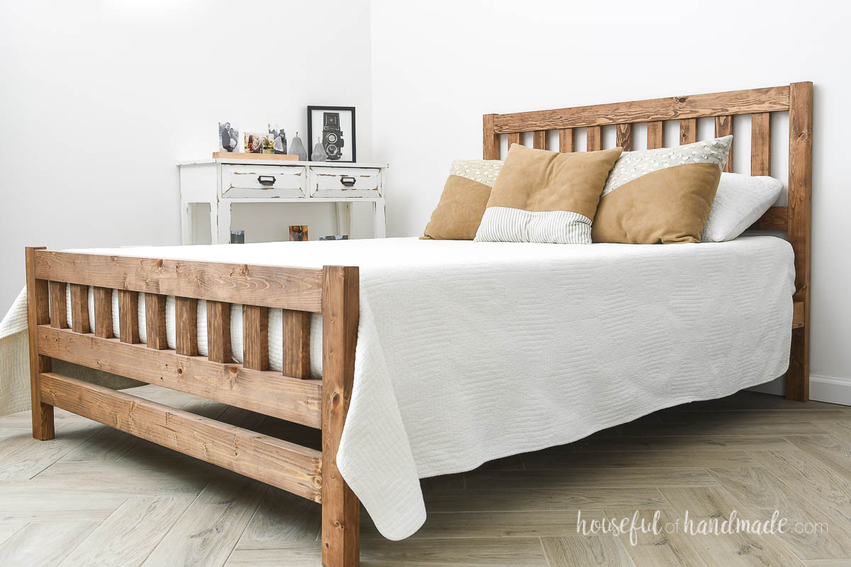 Full sized mission style wood bed with white bedding on a herringbone wood floor. 