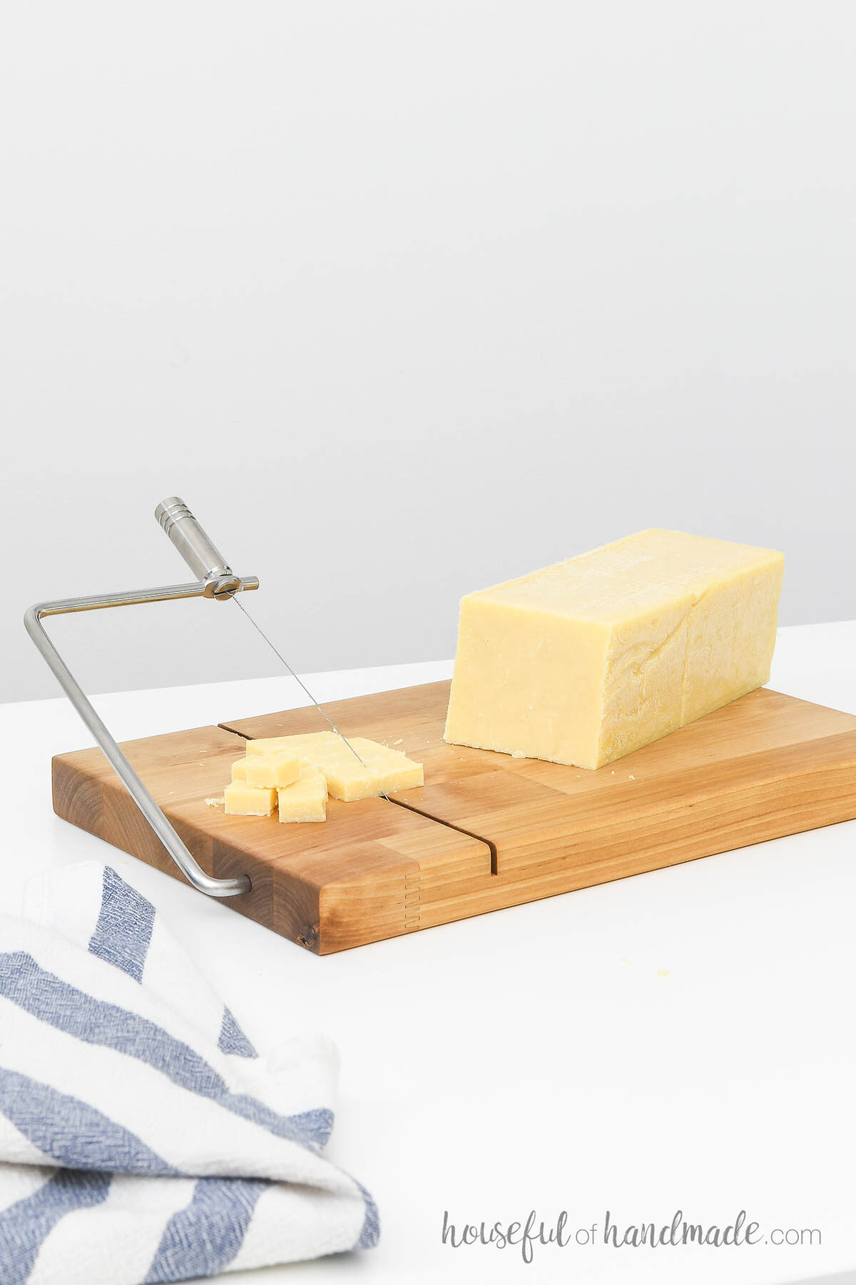 Butcher block DIY cheese slicer with a brick of cheese on it and a towel next to it. 