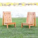 Two DIY modern adirondack chairs on the lawn in front of a lake.
