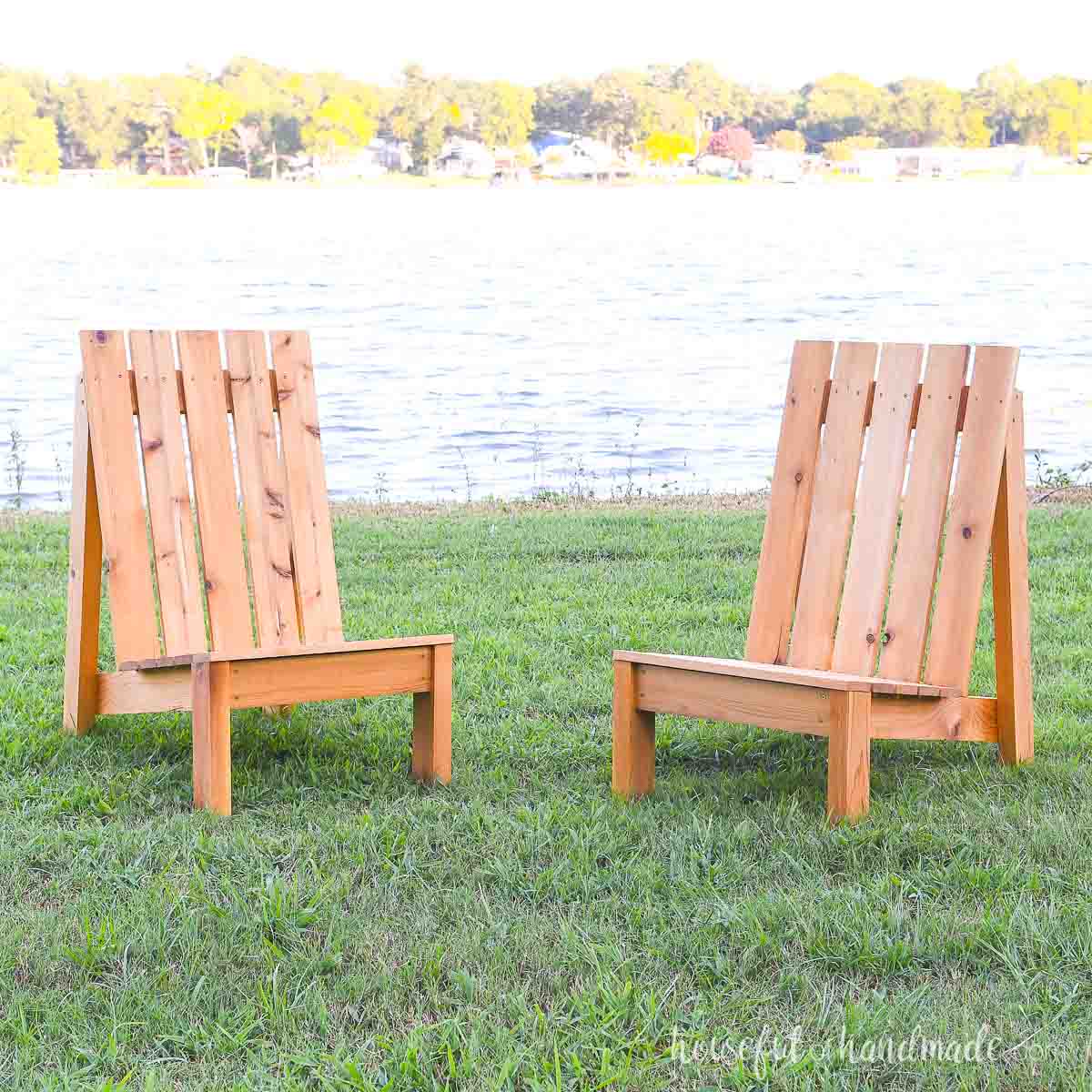 Two DIY modern adirondack chairs on the lawn in front of a lake.