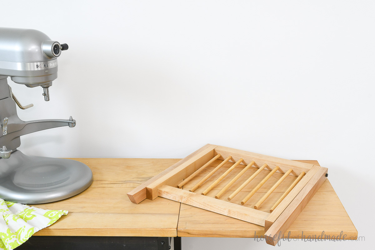 Pasta drying rack folded flat and laying on a table next to a mixer. 