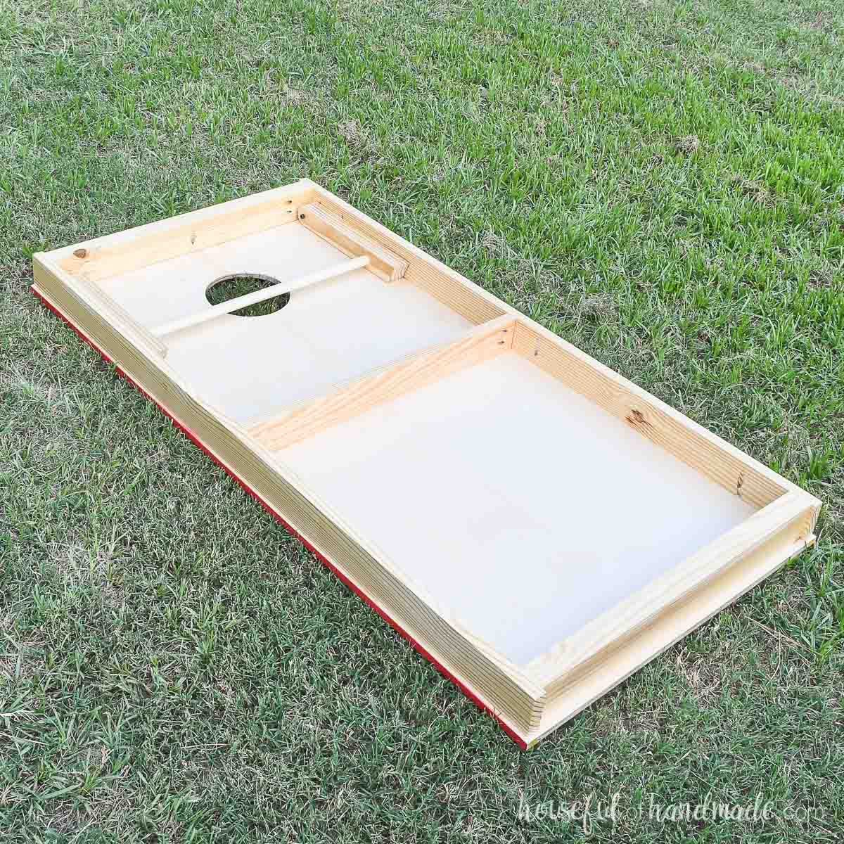 Wood cornhole board with legs folded inside the frame laying on the grass.