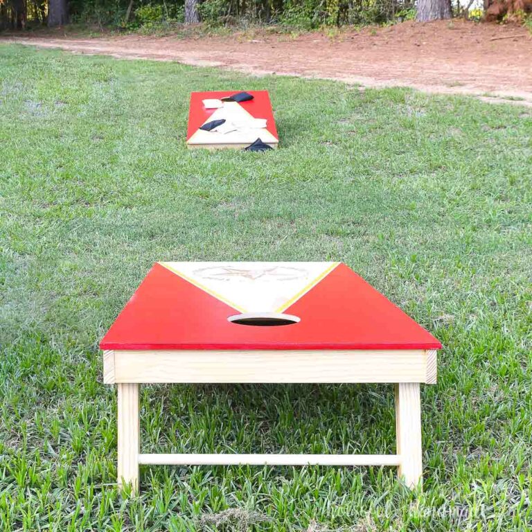 Two wood cornhole with custom design on the top set up on the grass.