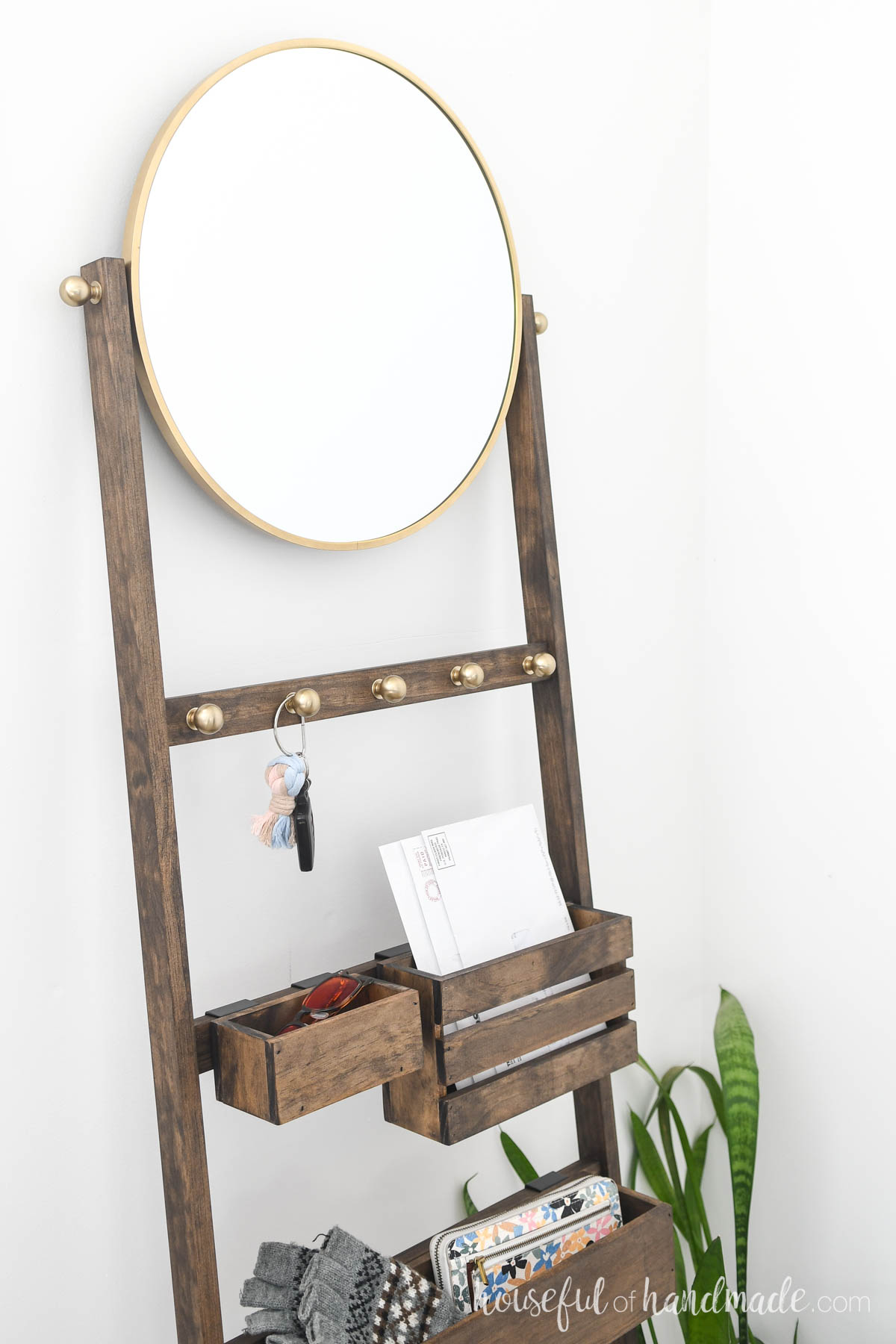 Ladder with round mirror on top and brass knobs for hooks. 