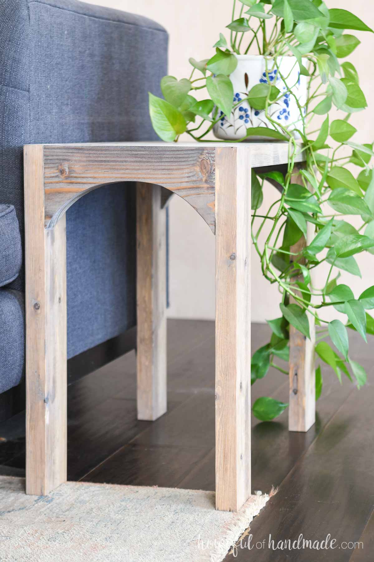 Slim side table with arch on the front next to a blue sofa. 