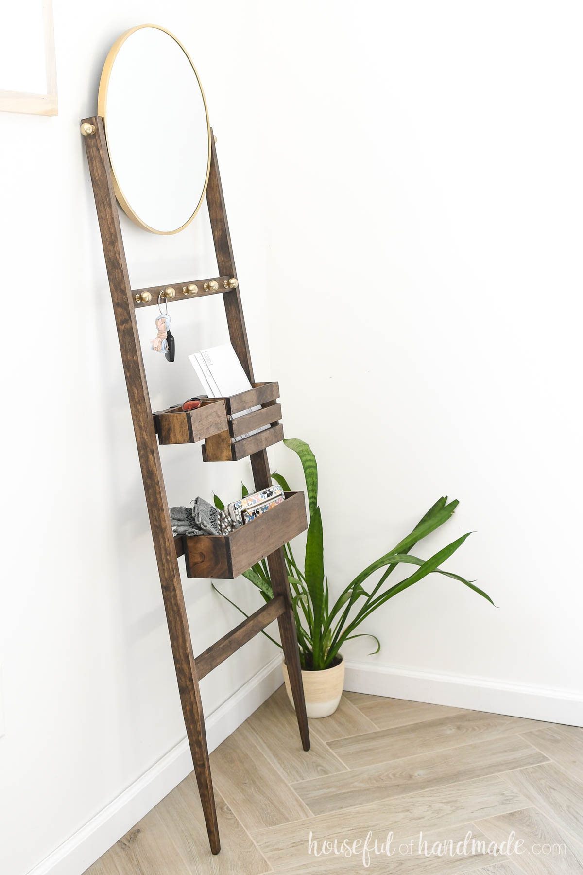 Walnut stained ladder for the entryway with bins and hooks and a mirror. 