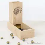 DIY dice tower made from poplar with a design on the front inside a tray.