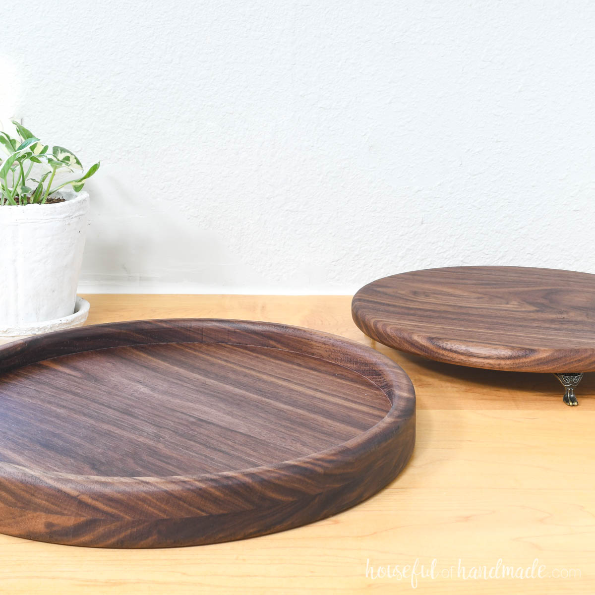 Two round wood trays, one with a lip creating a shallow bowl look, the other flat with legs. 