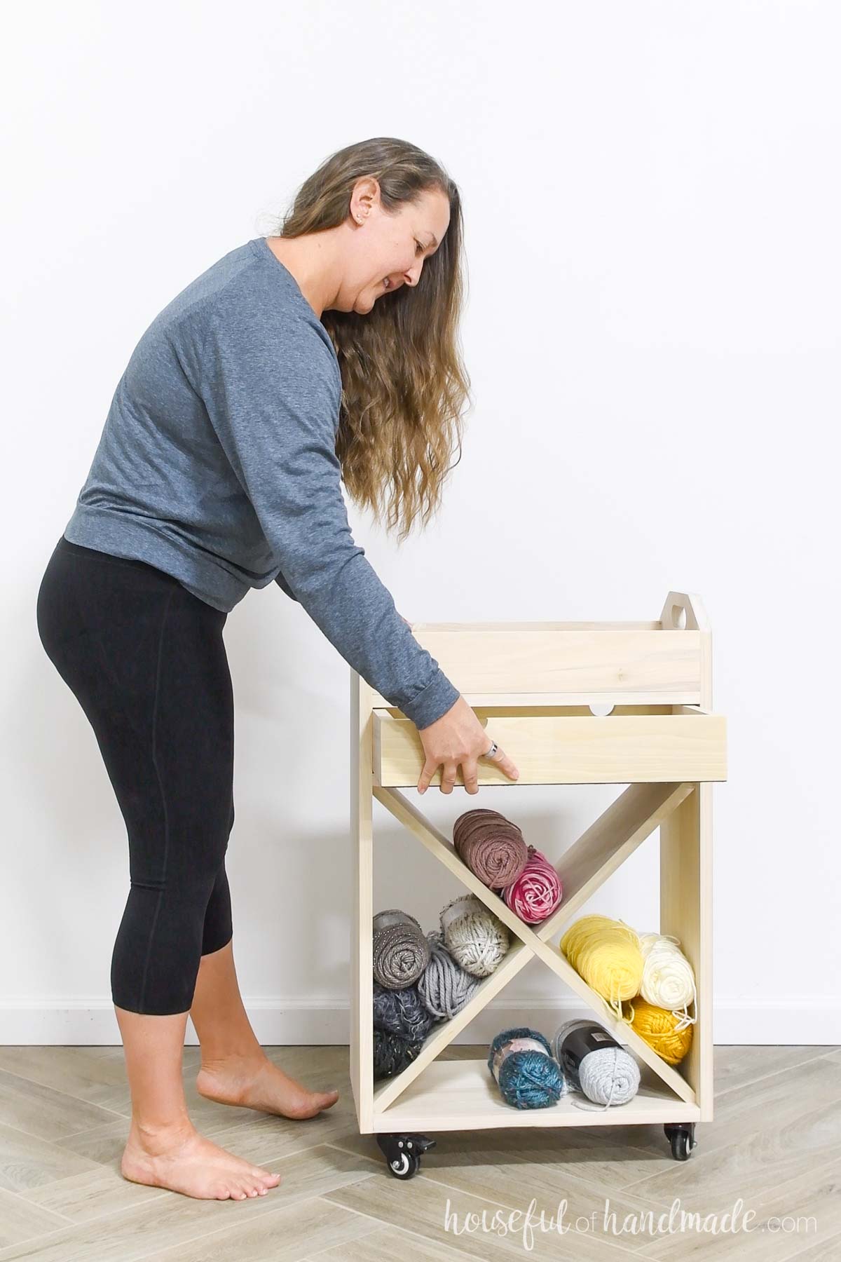 Kati standing nest to craft cart with yarn stored in the lower area opening the drawer. 