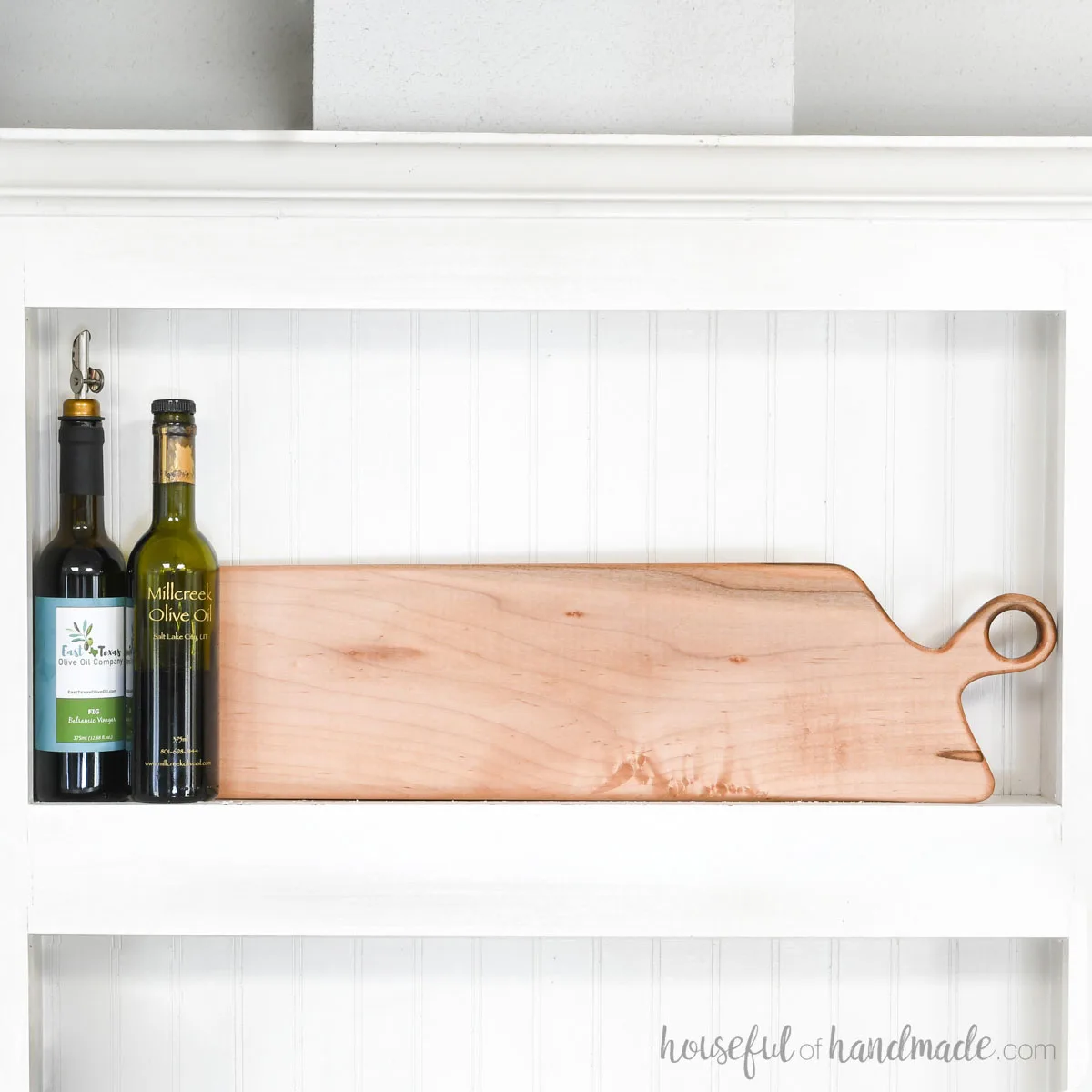 DIY long maple breadboard in a cubby with beadboard behind it and oils next to it.