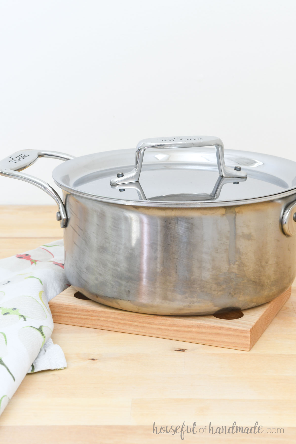 Stainless steel pot sitting on a light colored trivet made from wood. 