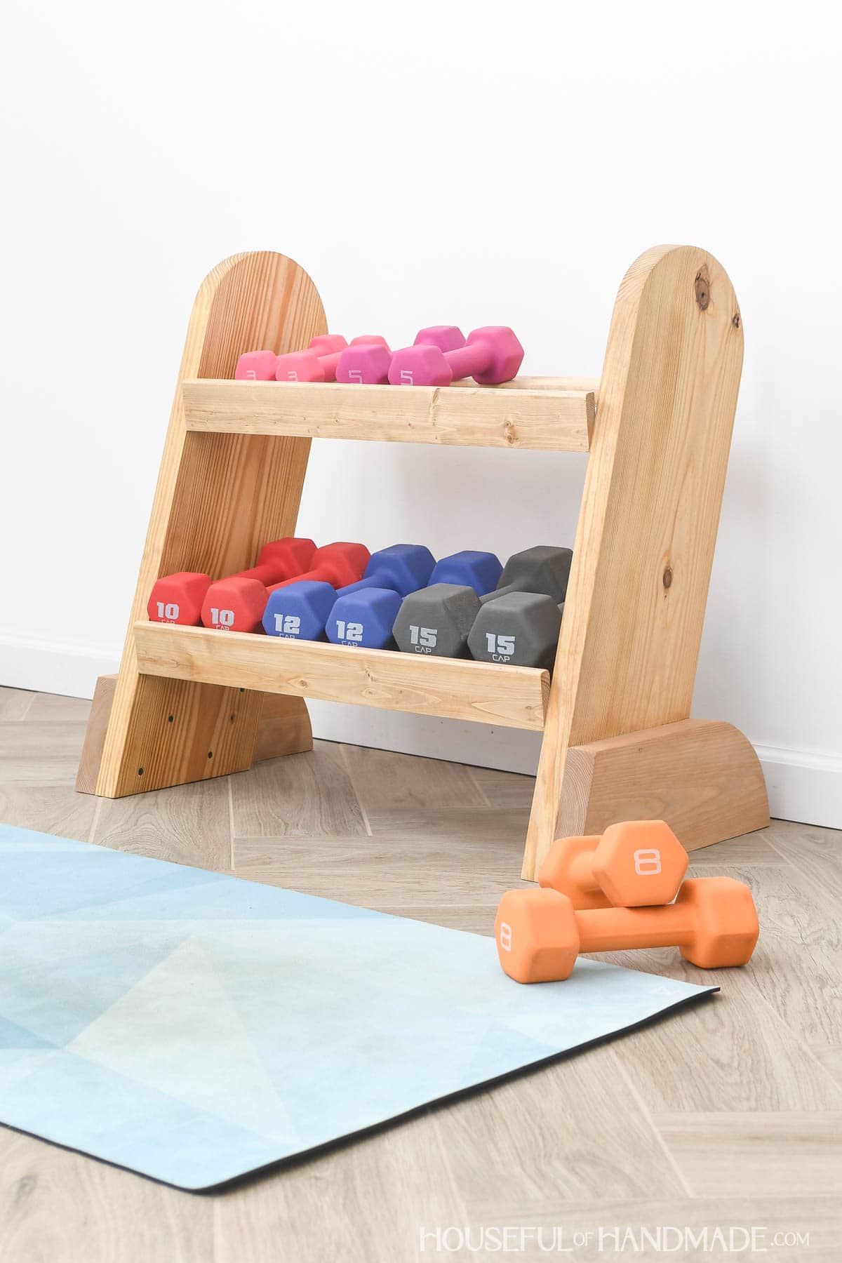 Wood weight rack with dumbbells on it and sitting next to it on the floor. 