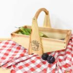 Large wooden harvest basket with mesh bottom sitting on a red picnic blanket.