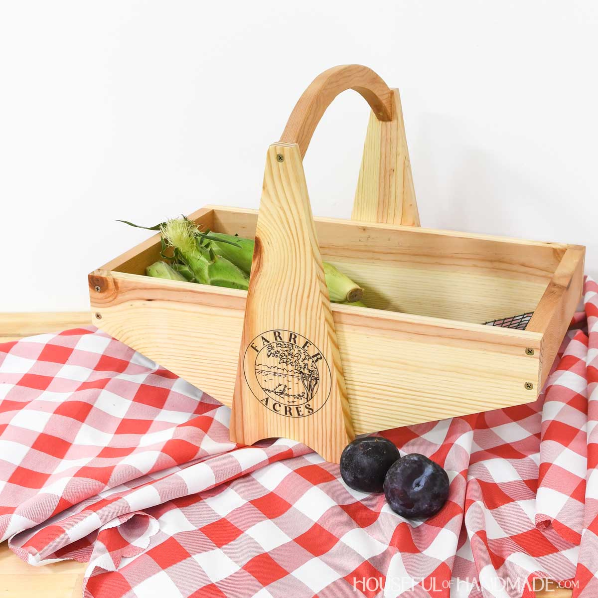Large wooden harvest basket with mesh bottom sitting on a red picnic blanket.