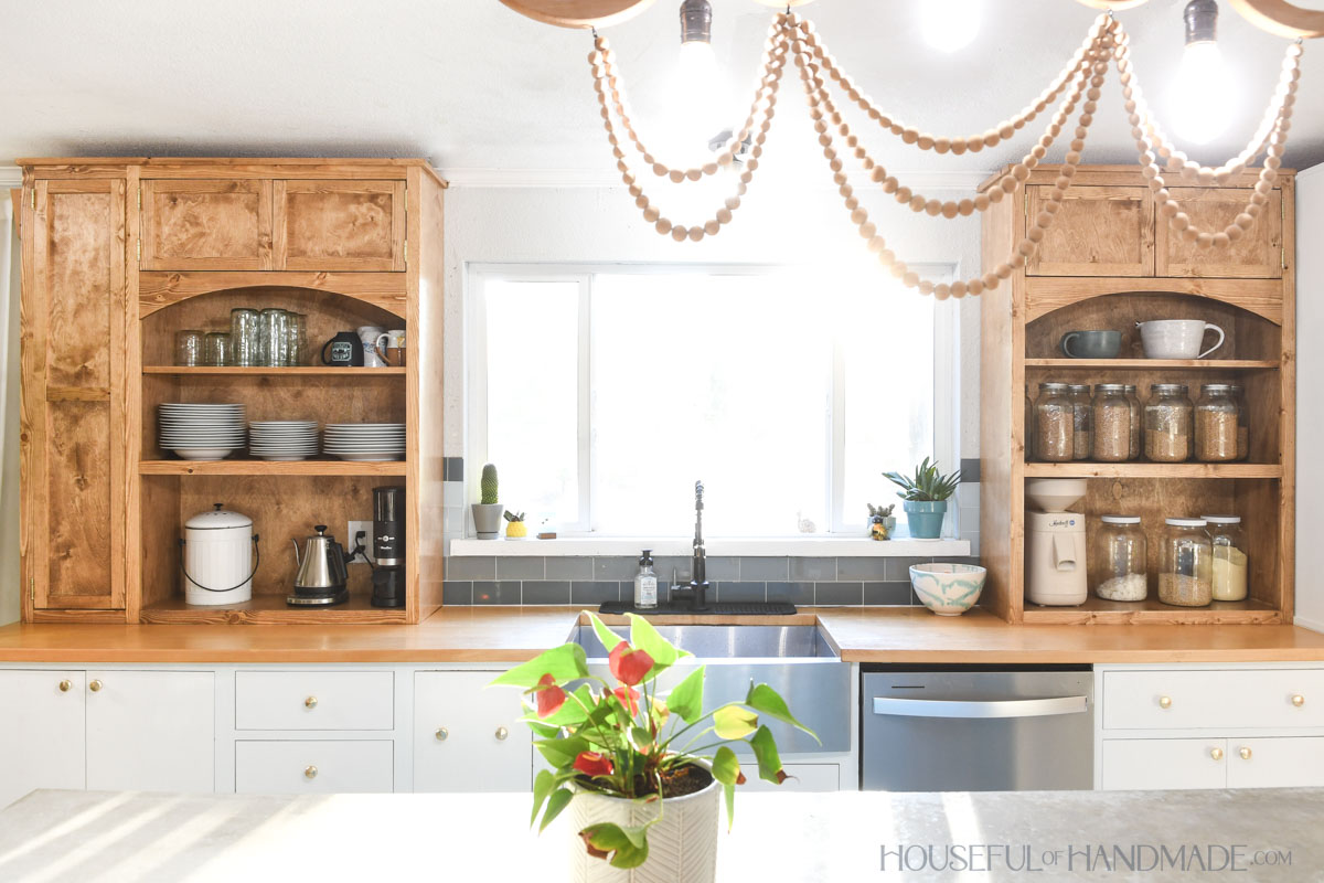 Kitchen with medium wood countertop cabinets on either side of the sink with large window between them. 