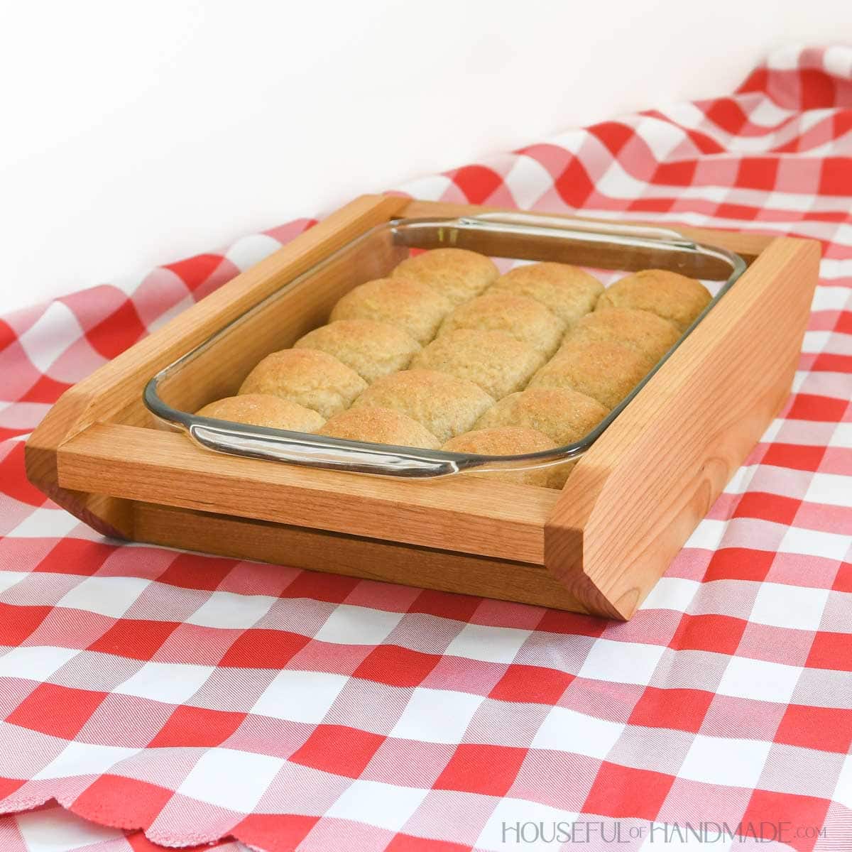 Side view of the wood casserole dish holder with a pan of homemade rolls inside.