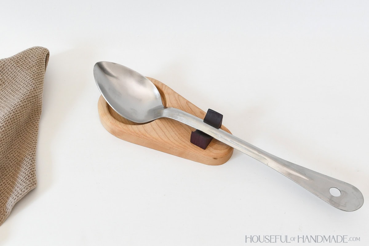 DIY wood spoon rest with large serving spoon on it next to towel.