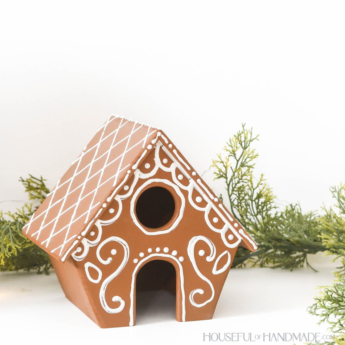 Small gingerbread house with angled sides made from wood and decorated with white paint. 