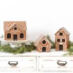 Three DIY wood gingerbread houses on a table with garland around them.