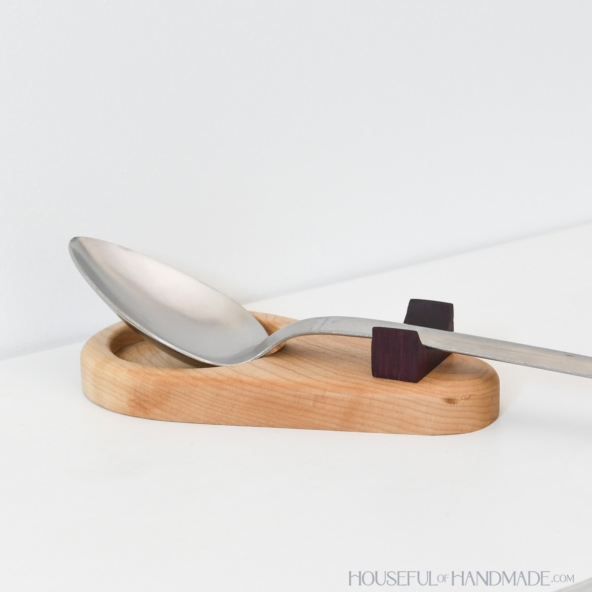 Maple and purple heart wood spoon rest with large metal spoon on it.