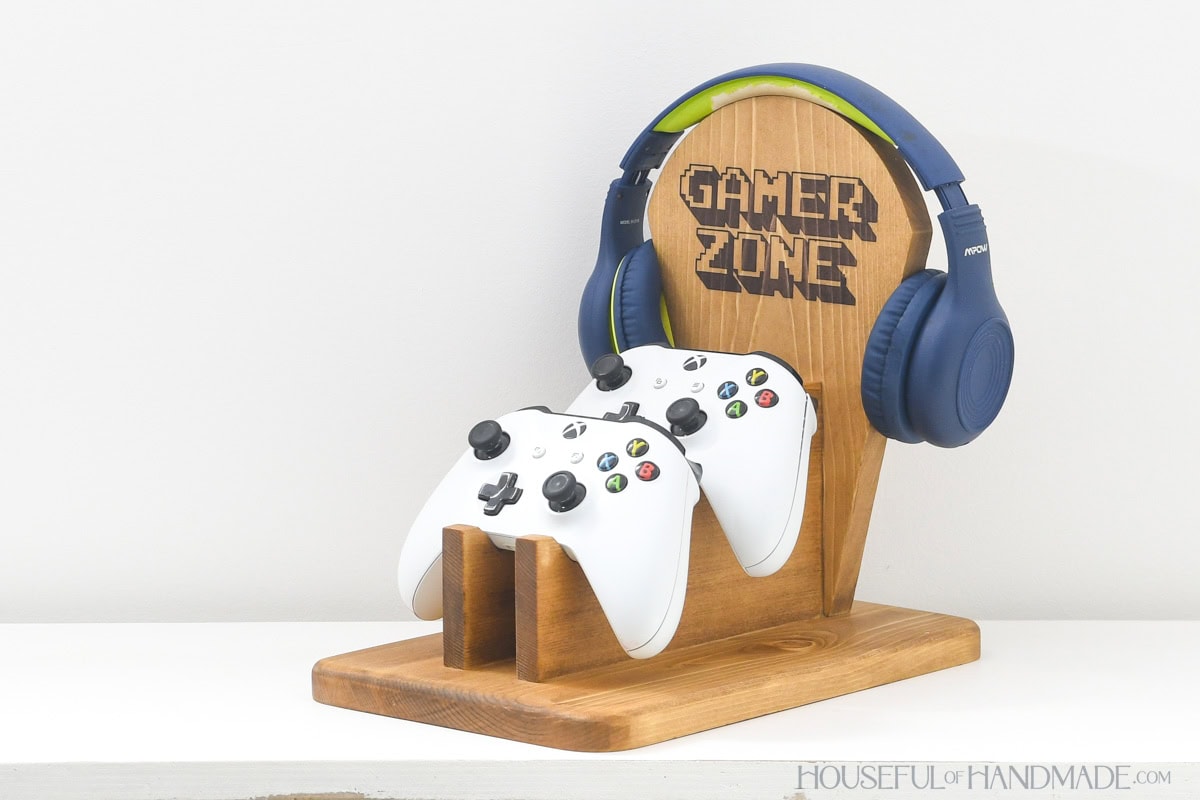 Side view of a solid wood stand with 2 game controllers on it.