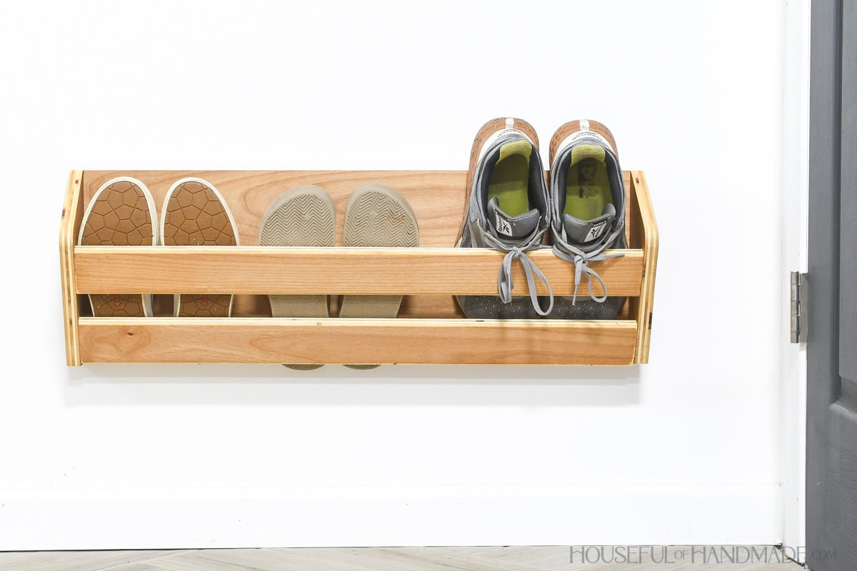 Three pair of shoes stored inside a wood shoe storage rack on a wall. 