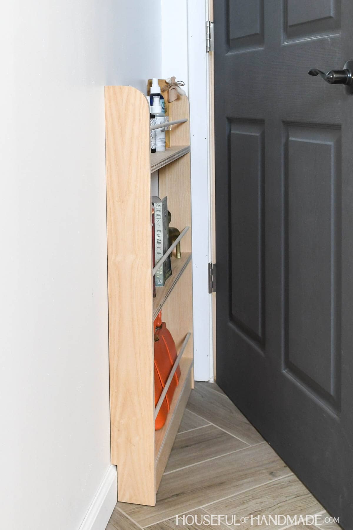 Behind the door shelf holding books, accessories, and hair products. 