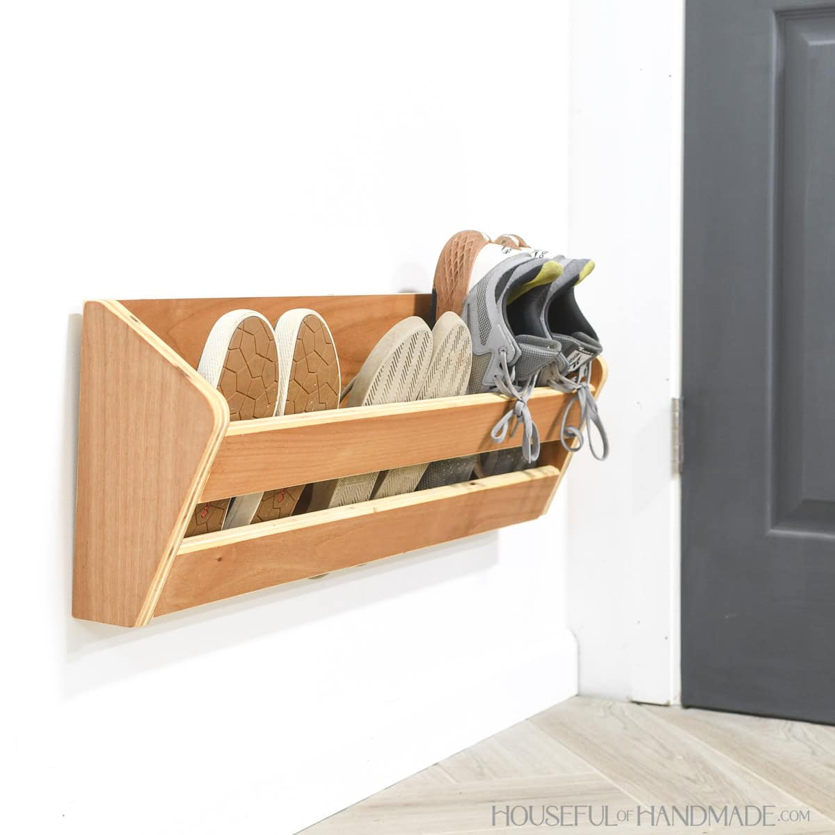 Wall mounted shoe rack built from scrap plywood hanging on the wall behind a door.