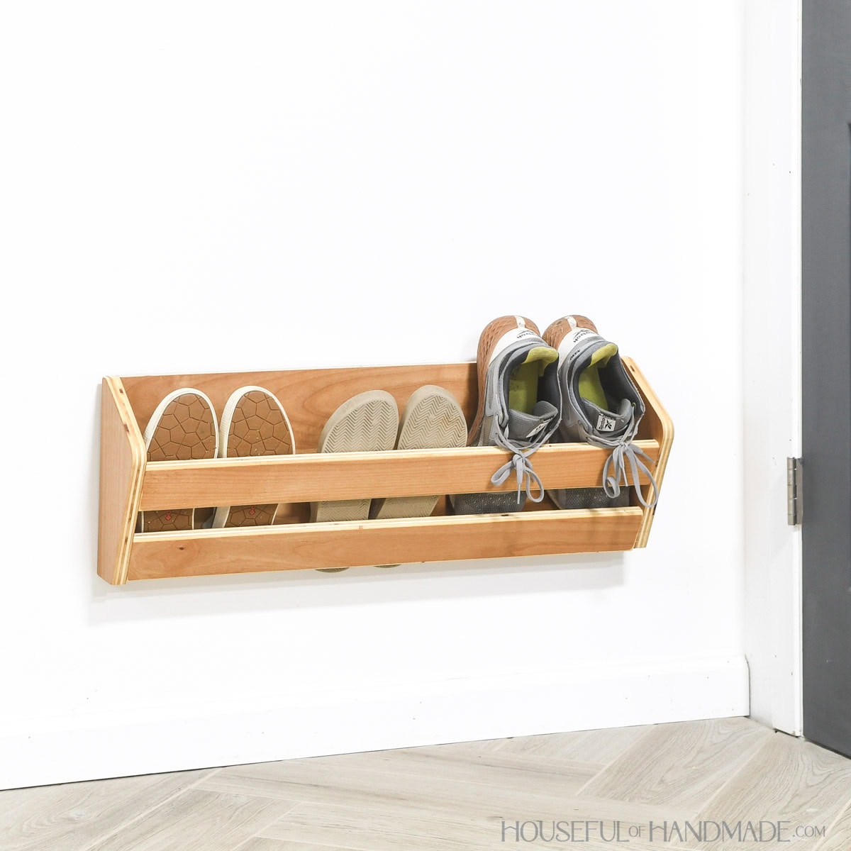 Shoe storage rack holding 3 pair of shoes mounted on a wall behind the door. 