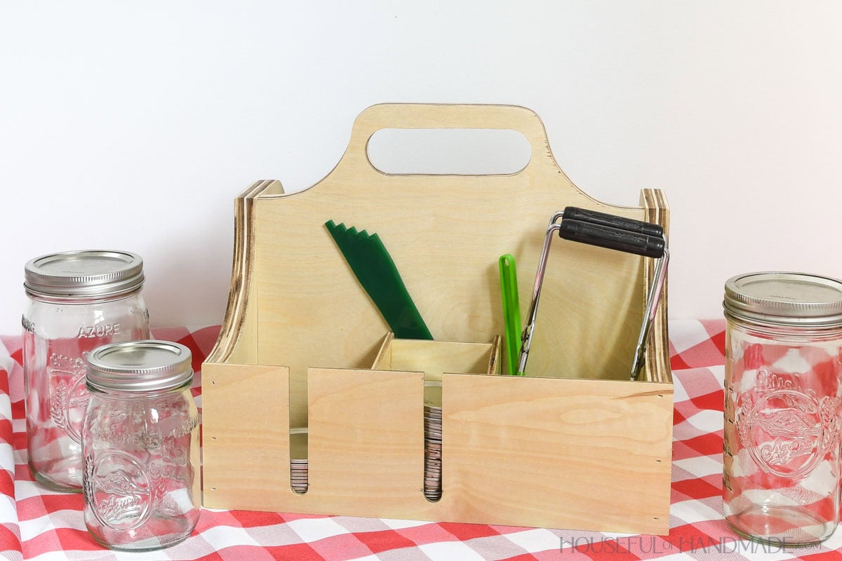 Front of the canning supply caddy with compartments for wide and regular mouth lids, head space ruler and jar lifter. 