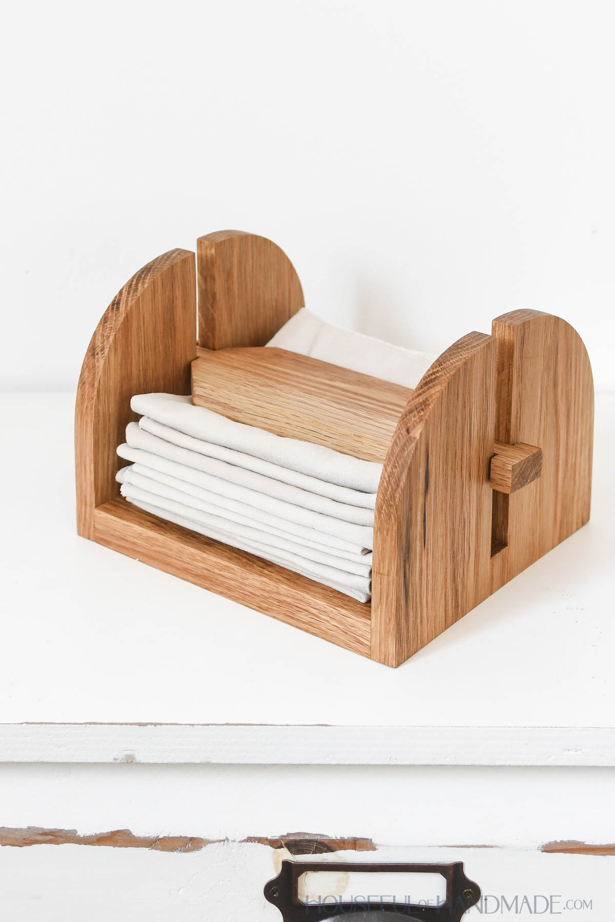 White oak wood napkin holder with top weight and cloth napkins inside. 
